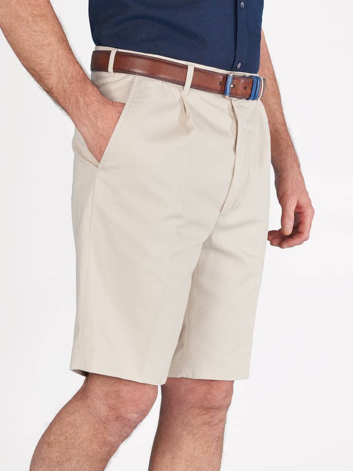 Das Model trägt eine beigefarbene Plisseeshorts aus Baumwolle für Herren.